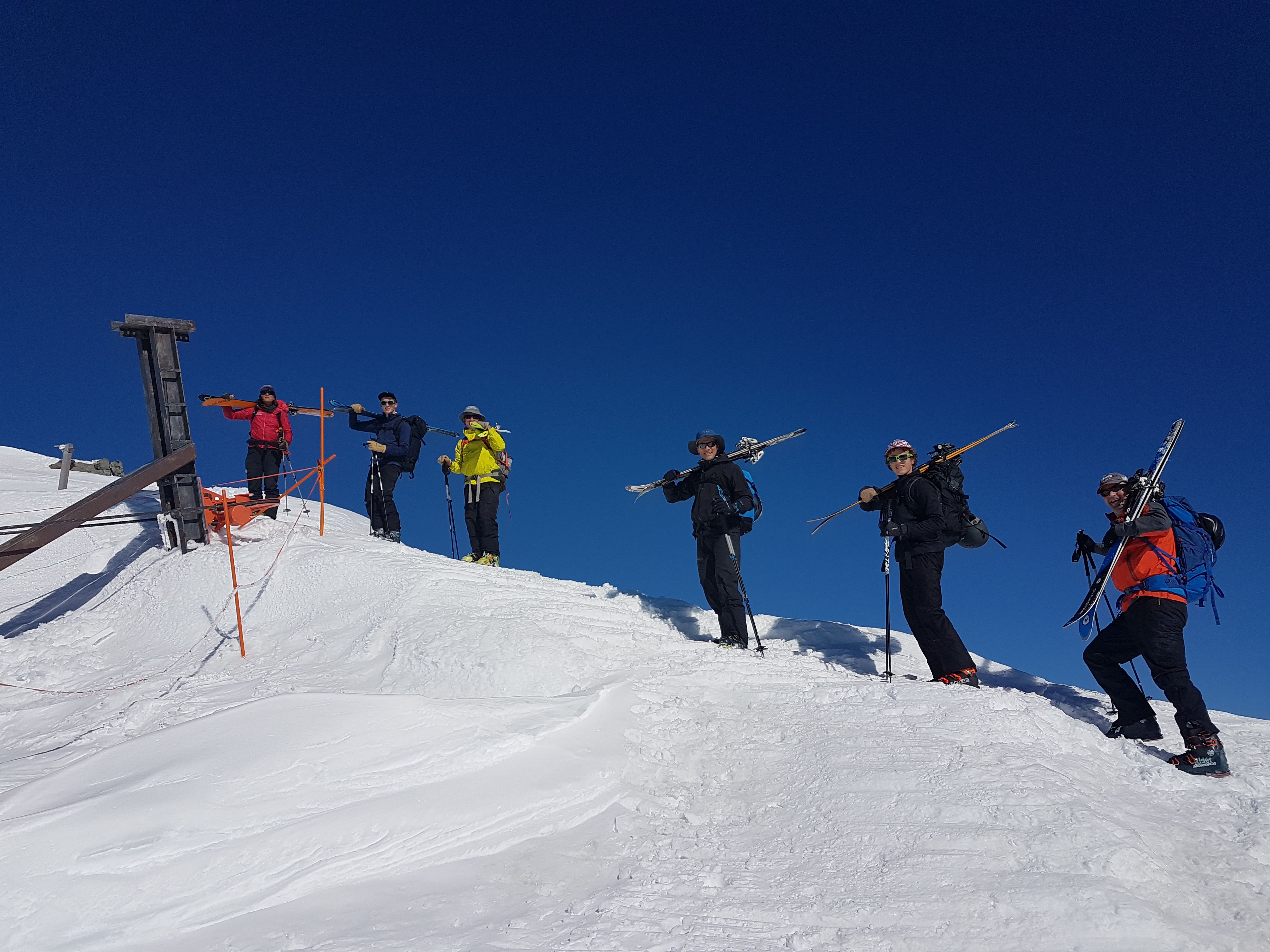 6 people walking up snowy ridge carrying skis