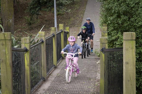 Dad and children riding bicycles, crossing the bridge, wearing helmets