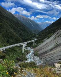 A bridge and river crossing in the middle of beautiful Mountains, clouds in the sky
